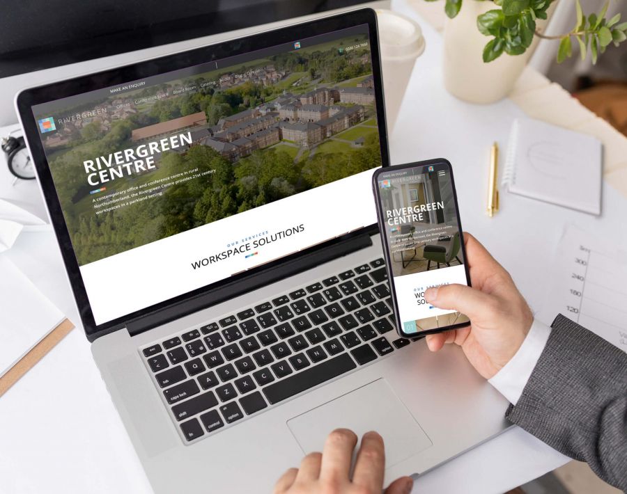 person holding phone with infront of laptop, looking at Rivergeen Centre website