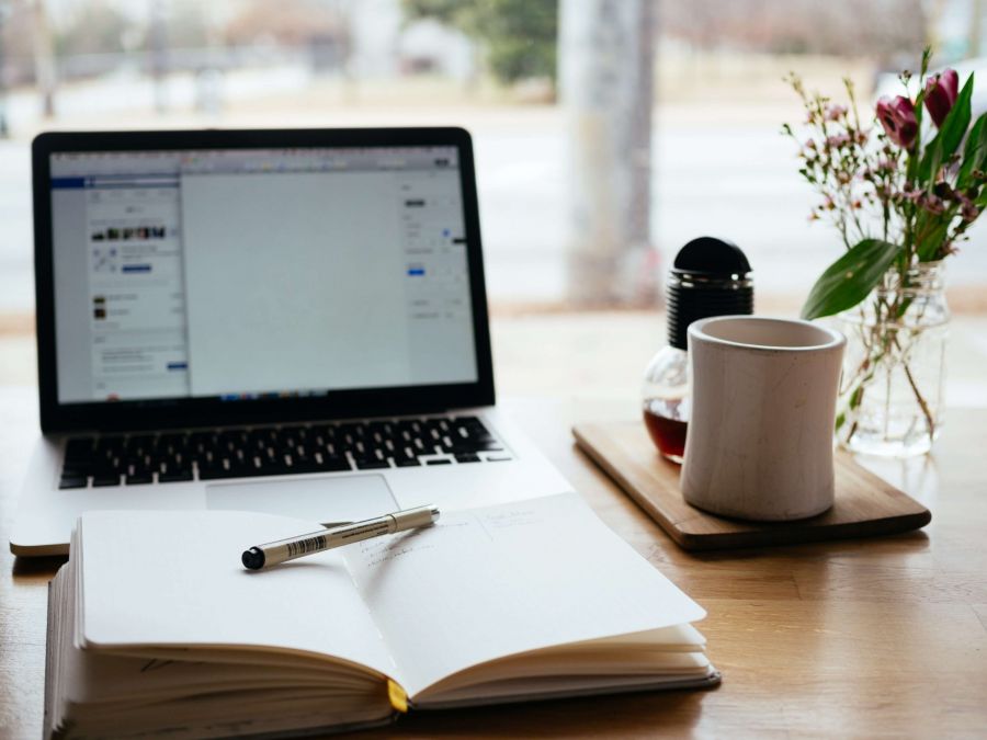 pencil on an open notebook with a laptop in the background on a desk